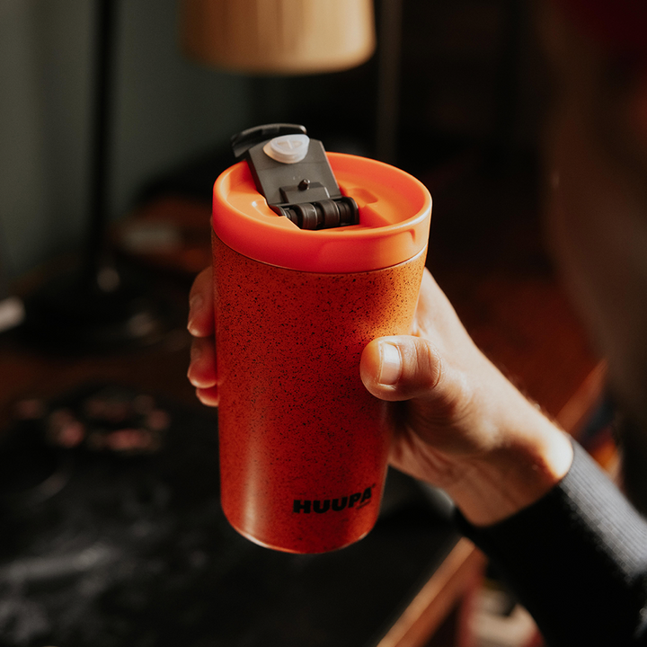 Hand holding an orange thermos with a blurred indoor background