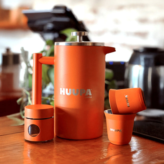 Orange HUUPA coffee press and cups on a wooden surface with a blurred kitchen background