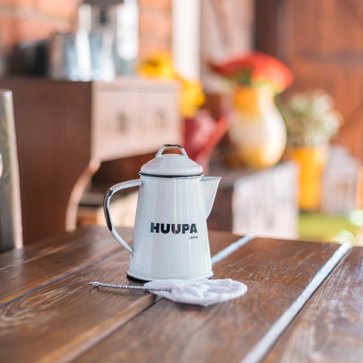 White coffee pot with 'HUUPA' branding on a wooden table in a kitchen setting.