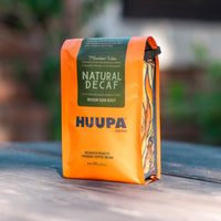 Orange Natural Decaf Huupa Coffee bag with green label on a wooden surface