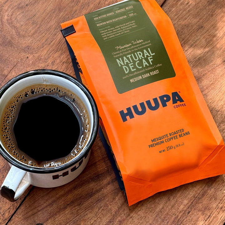 Orange Huupa Coffee package next to a cup of coffee on a wooden surface