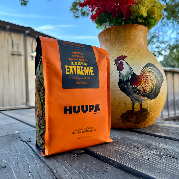 Orange Huupa Coffee Extreme bag on a wooden surface with a decorative vase featuring a rooster.