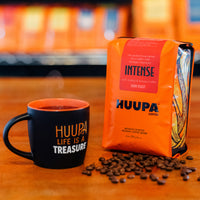 HUUPA coffee bag and mug on a wooden surface with blurred background