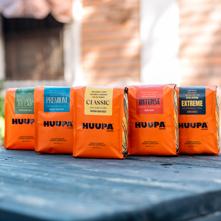 Huupa Sampler, five orange Huupa coffee bags with blurry background and wooden table: natural decaf, premium, classic intense and extreme.