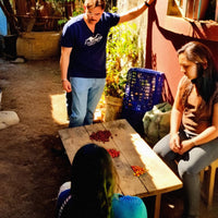 Two people sitting at a wooden table with red berries on it, outdoors. Enrique Lopez and Women Coffee producers working.