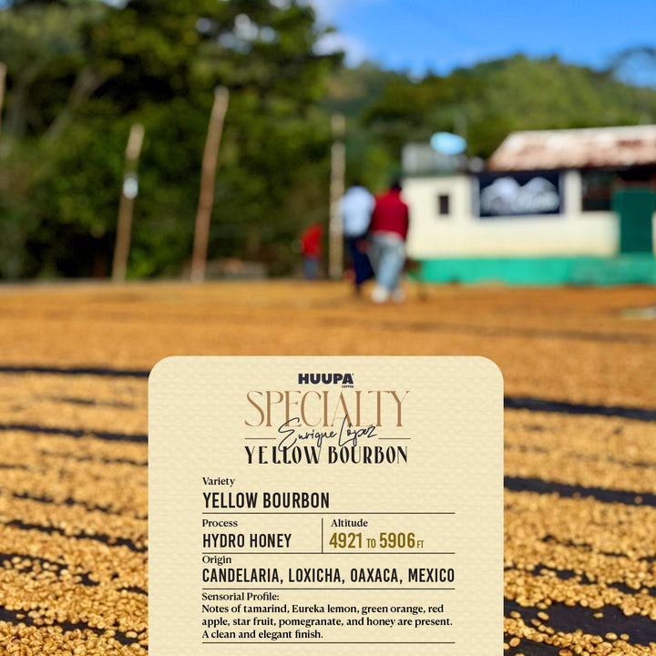 A close-up of a beige product label for HUAPA Specialty Yellow Bourbon whiskey, set against a blurred outdoor background of a coffee bean field and workers.