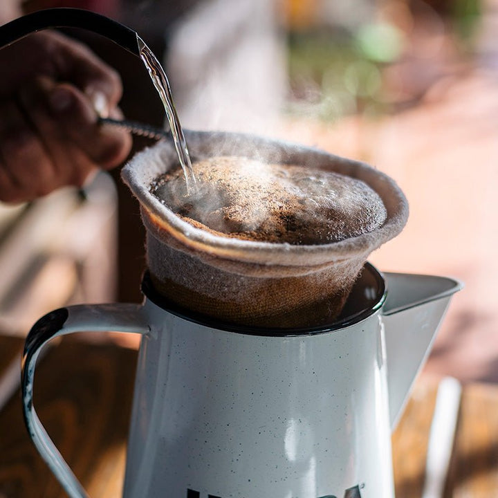 Hand pouring liquid into a coffee filter over a white pitcher.